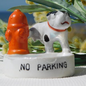 Op de afbeelding: Een wit keramiek beeldje van een hond en een brandkraan op een witte basis met de tekst "NO PARKING" erop.