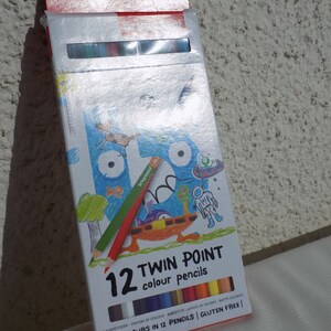K&ouml;nnte beinhalten: Eine Schachtel mit 12 doppelseitigen Farbstiften mit 24 Farben. Die Schachtel zeigt eine Comic-Illustration eines Monsters mit einem gr&uuml;nen, roten und blauen Stift im Maul. Auf der Schachtel steht "12 Twin Point Farbstifte" und "24 Farben in 12 Stiften | Glutenfrei".