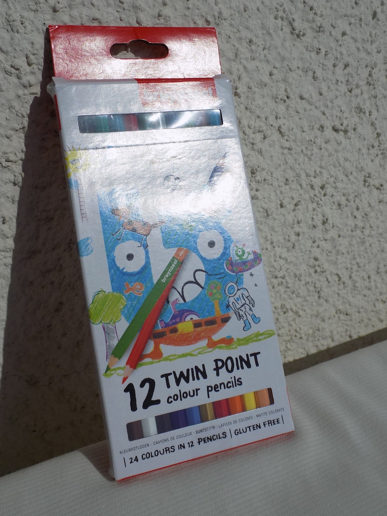 K&ouml;nnte beinhalten: Eine Schachtel mit 12 doppelseitigen Farbstiften mit 24 Farben. Die Schachtel zeigt eine Comic-Illustration eines Monsters mit einem gr&uuml;nen, roten und blauen Stift im Maul. Auf der Schachtel steht "12 Twin Point Farbstifte" und "24 Farben in 12 Stiften | Glutenfrei".