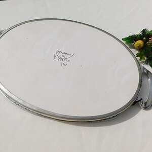 May include: A silver oval serving tray with two handles. The tray has a white ceramic insert with the words "Magnum HN 9elria 7in" written in purple ink.