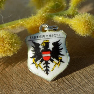 K&ouml;nnte beinhalten: Ein kleiner, schildf&ouml;rmiger Anh&auml;nger mit dem Wort "&Ouml;STERREICH" oben. Der Anh&auml;nger zeigt das &ouml;sterreichische Wappen: einen schwarzen Adler mit einem rot-wei&szlig;em Schild auf der Brust. Der Anh&auml;nger hat einen silberfarbenen Rand und eine kleine Schlaufe oben.
