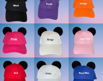 May include: Nine baseball caps with Mickey Mouse ears in different colours: black, purple, orange, pink, beige, light pink, red, white, and royal blue. Each cap has the colour name printed on the front.