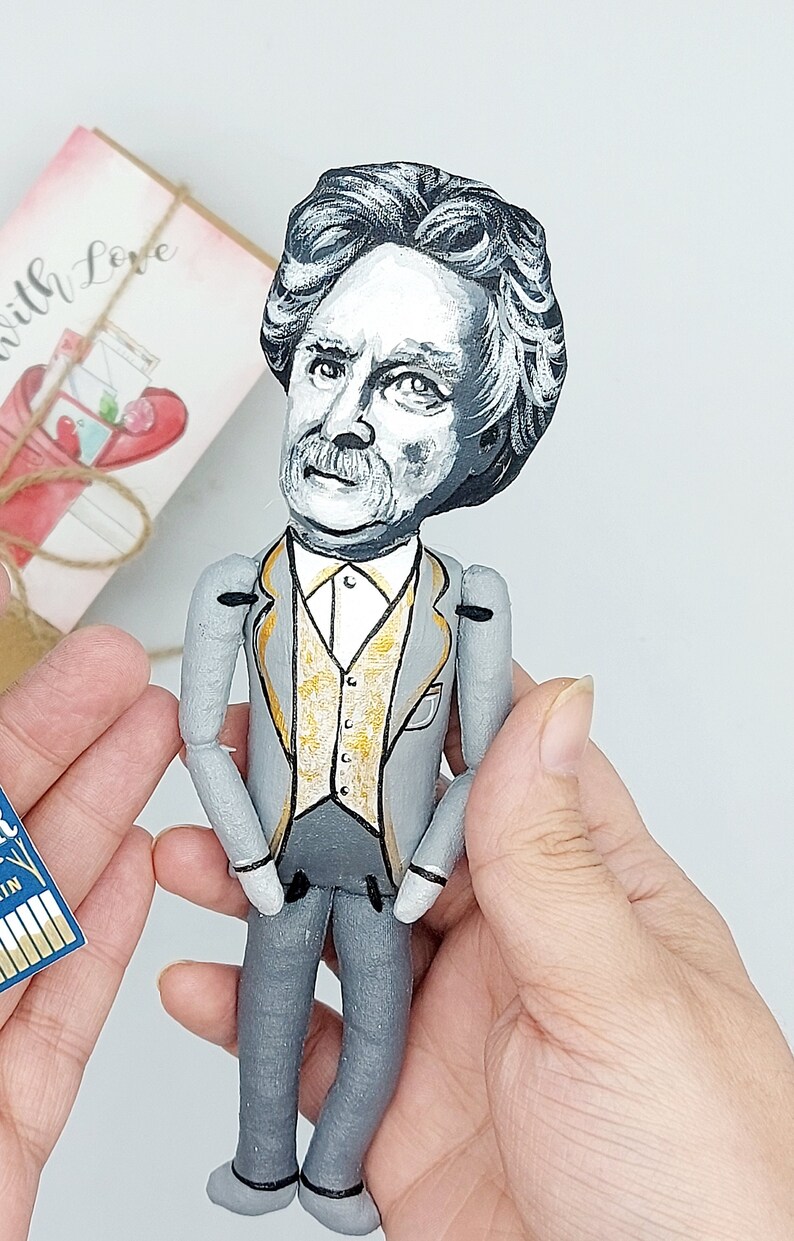 May include: A hand-painted doll of a man with gray hair and a mustache, wearing a gray suit with a gold vest. The doll is holding its hands in front of its waist.