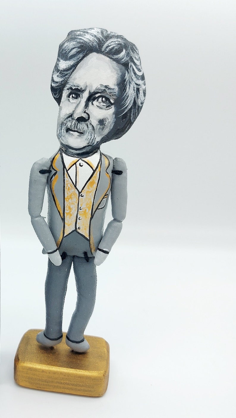 May include: A hand-painted wooden figurine of a man with gray hair and a mustache, wearing a gray suit with a gold vest. The figurine is standing on a gold base.