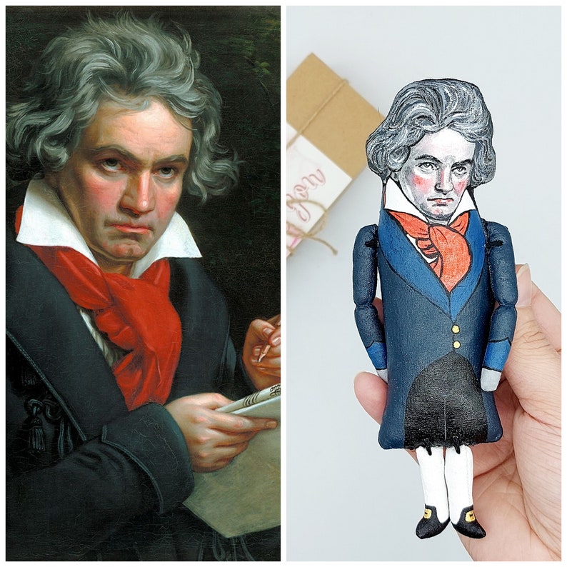 May include: A hand-painted doll of a man wearing a blue suit with a red scarf and a white collar. The doll has brown hair and a serious expression.