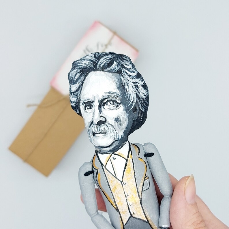May include: A hand-painted doll of a man with a black and white portrait style face and a gray suit with a gold vest. The doll has a mustache and a dark brown hair.