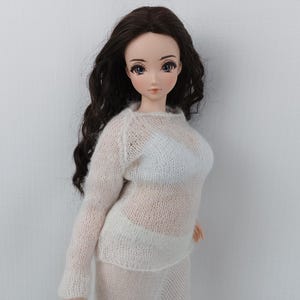 May include: A doll with long, dark brown wavy hair, dressed in a sheer, off-white knit sweater and skirt. The doll has a fair complexion, with detailed facial features and blue eyes. The outfit appears to be handmade.