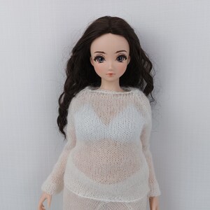 May include: A doll with long, dark brown wavy hair and blue eyes. The doll is wearing a sheer, white knit sweater and a matching skirt. The doll's skin is pale, and it has a neutral expression.