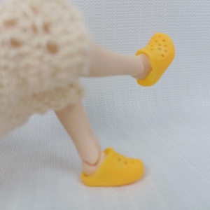 Può includere: Un paio di scarpe per bambole gialle con un design testurizzato. Le scarpe sono realizzate in un materiale morbido e flessibile.
