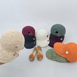 May include: A set of six crocheted hats in various colors, including beige, orange, green, navy blue, burgundy, and white. Each hat has a small flower-shaped embellishment and a button on the side. There are also two pairs of crocheted sandals in orange and white.