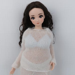 May include: A doll with long, dark brown hair and blue eyes, dressed in a sheer white sweater and skirt. The doll's outfit includes a white bra. The doll is set against a plain white backdrop.