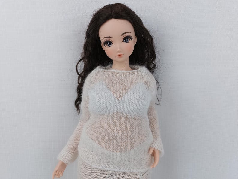 May include: A doll with long, dark brown hair and blue eyes, dressed in a sheer white sweater and skirt. The doll's outfit includes a white bra. The doll is set against a plain white backdrop.