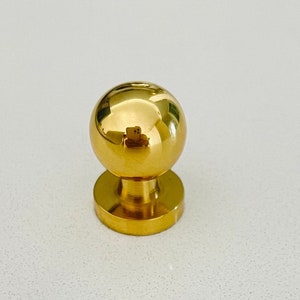 May include: A gold-toned round cabinet knob with a smooth, shiny finish.