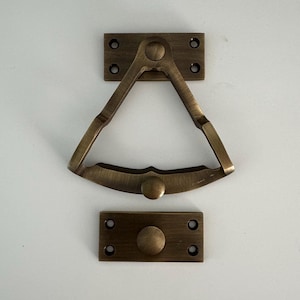 Puede incluir: Un pestillo de puerta de latón con forma triangular y un pomo redondo. El pestillo está unido a una placa rectangular con dos tornillos.