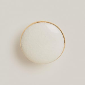 Puede incluir: Perilla de armario redonda de cerámica blanca con efecto craquelado. Tiene un fino borde metálico dorado. Ideal para muebles y decoración del hogar.