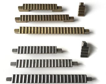 May include: A set of six decorative cabinet pulls in two finishes. Three pulls are a brushed nickel finish and three pulls are a brass finish. The pulls have a ribbed design and are rectangular in shape.