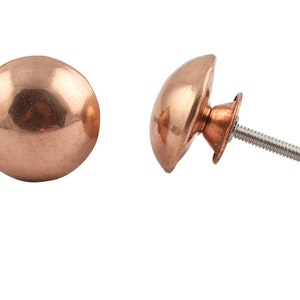 May include: Two copper cabinet knobs, one with a screw and the other without. The knobs are round and have a smooth, shiny finish.