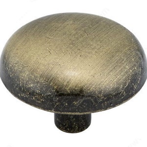 May include: A round, antique brass cabinet knob with a mushroom-shaped design. The knob has a distressed finish and a slightly raised center.