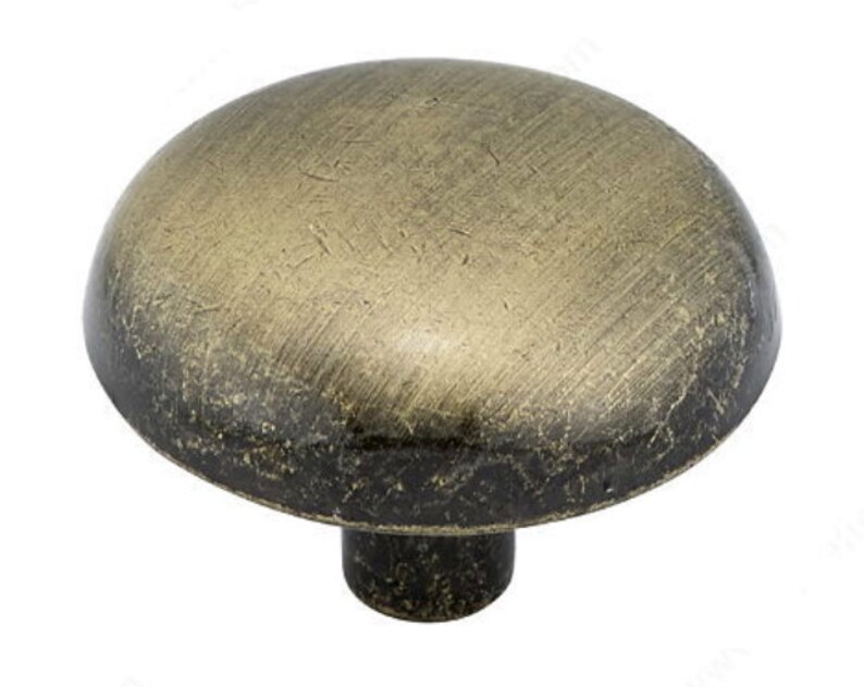 May include: A round, antique brass cabinet knob with a mushroom-shaped design. The knob has a distressed finish and a slightly raised center.