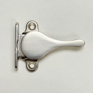 Puede incluir: Un pestillo de puerta plateado con una manija de palanca. El pestillo está diseñado para montarse en una puerta y tiene un diseño simple y moderno.