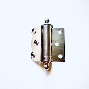 Puede incluir: Una bisagra de puerta plateada con la parte superior e inferior redondeadas. La bisagra tiene cuatro agujeros a cada lado para sujetarla a una puerta y al marco de la puerta.