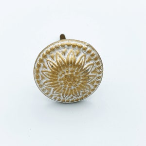 May include: A gold and white round cabinet knob with a floral design.