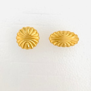 May include: A pair of gold-tone earrings with a textured, scalloped design. The earrings are round and oval in shape.