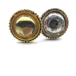 May include: Two round, decorative cabinet knobs with a gold and silver finish. The knobs have a beaded edge and a raised, circular center.