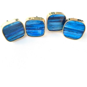 May include: Four square cabinet knobs with a brass frame and a blue and white striped inlay.