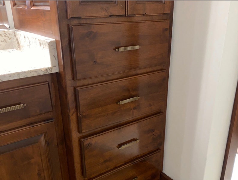May include: A set of five wooden drawers with brushed gold hardware. The drawers are in a bathroom vanity and are made of a dark wood.