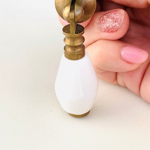 May include: White ceramic cabinet knob with a brass base and a decorative ring around the bottom. The knob is shaped like a teardrop.