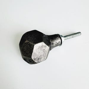 May include: A silver and black metal cabinet knob with a geometric shape and a screw.