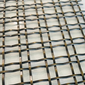May include: A close-up of a woven metal mesh with a bronze finish. The mesh is made of thin, interwoven wires that create a grid pattern.