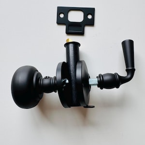 May include: A matte black door handle set with a round knob and a lever. The set includes a matching rectangular strike plate and a threaded spindle. The hardware is designed for interior doors.