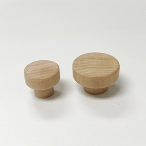 May include: Two wooden knobs, one larger than the other, with a round top and a cylindrical base. The knobs are a light brown colour and have a smooth, polished finish.