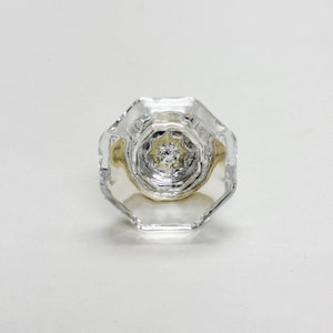 Può includere: Un anello di vetro trasparente con una montatura in oro e un grande diamante sfaccettato al centro.