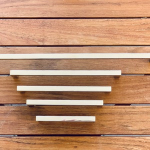 Peut inclure: Cinq poignées de tiroir argentées de différentes longueurs disposées en forme de pyramide sur une surface en bois.