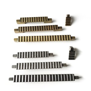 May include: Set of six gold and silver cabinet pulls with a ribbed design. The pulls are in various sizes and are arranged in two rows.