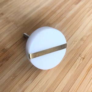 May include: White round cabinet knob with a gold metal band across the center.