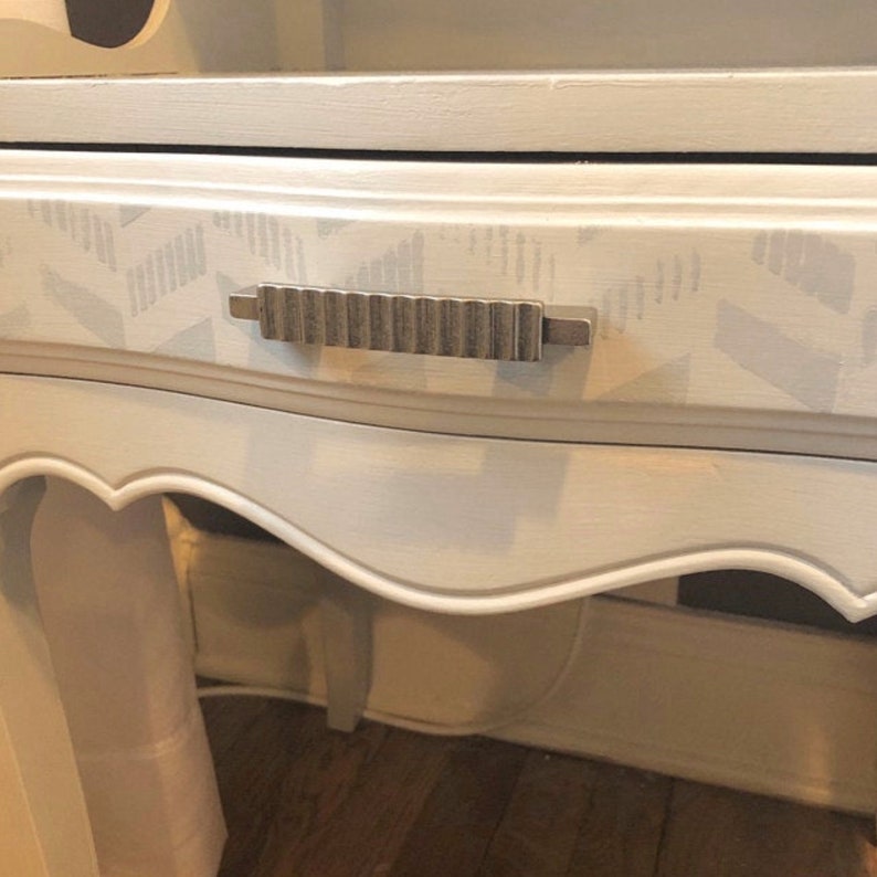 May include: A white nightstand with a drawer and a silver drawer pull. The drawer has a gray and white geometric pattern.