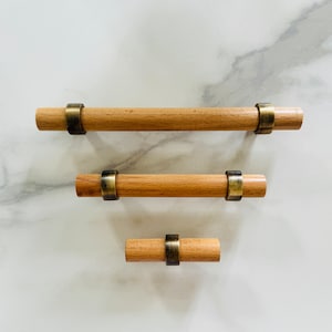 May include: Three wooden drawer pulls with brass accents. The pulls are different sizes and are arranged in a vertical line.