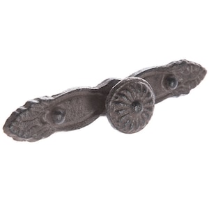 May include: A cast iron drawer pull with a decorative floral design. The pull is dark brown and has a knob in the center.