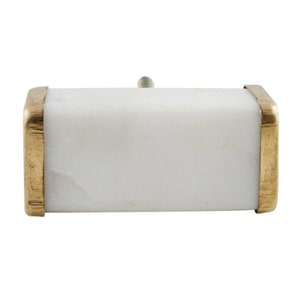 May include: White marble drawer pull with a brass trim. The pull is rectangular in shape and has a slightly rounded edge.
