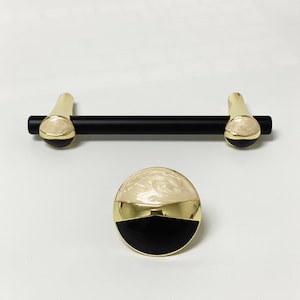 May include: A set of two black and gold cabinet knobs with a white marbled design. The knobs are round and have a flat back.