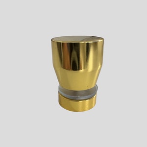 May include: Gold metal bottle stopper with a clear glass base. The stopper has a smooth, shiny finish.