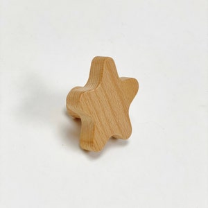 May include: A wooden star-shaped knob in a light brown color. The knob has a smooth, rounded surface and is perfect for adding a touch of whimsy to furniture or decor.