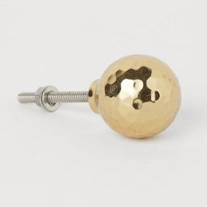 Puede incluir: Un pomo de armario de cerámica de color dorado con un acabado martillado y un tornillo plateado.