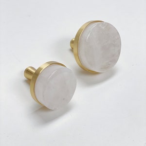 May include: Two round, white, natural stone drawer pulls with a gold metal rim. The pulls are different sizes.
