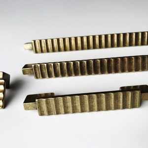 May include: Four antique gold-toned cabinet pulls with a ridged design. The pulls are in various sizes and shapes.