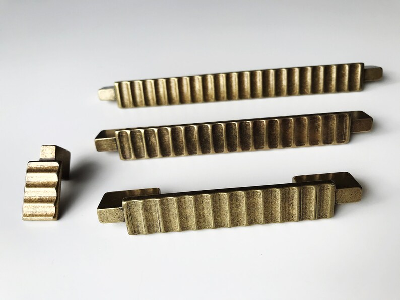 May include: Four antique gold-toned cabinet pulls with a ridged design. The pulls are in various sizes and shapes.